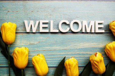 Tahta arka planda sarı lale çiçekli alfabeye hoş geldiniz.