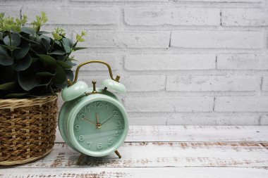 Ahşap ve beyaz tuğla duvar zemininde yeşil alarm saati ve yapay bitki süslemesi