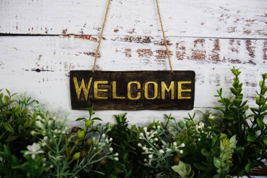 Hoş geldin işareti asılı halat ve yeşil yapay bitki ahşap arka planda