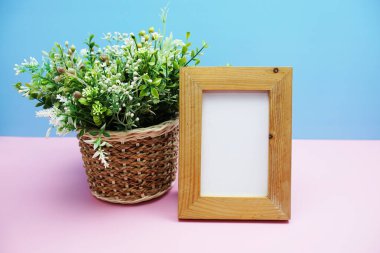 Pembe ve mavi arka planda yeşil yapay bitki içeren boş ahşap çerçeve