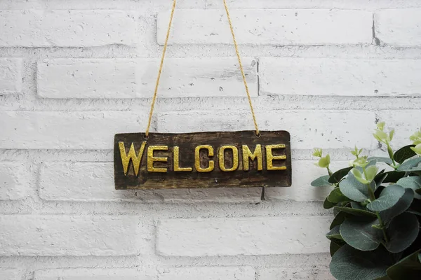 Welcome sign hanging with rope on white brick wall background