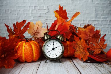 Ahşap zemin üzerinde balkabağı ve akçaağaç yaprağı olan çalar saat.