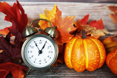 Ahşap zemin üzerinde balkabağı ve akçaağaç yaprağı olan çalar saat.