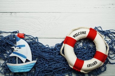 Denizcilik yelkenli oyuncak model ve ahşap arka planda mavi balıkçı ağı manzaralı can simidi.