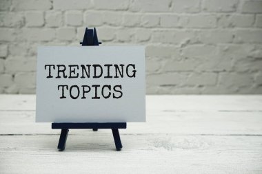 Trending Topics text on white brick wall and wooden background clipart