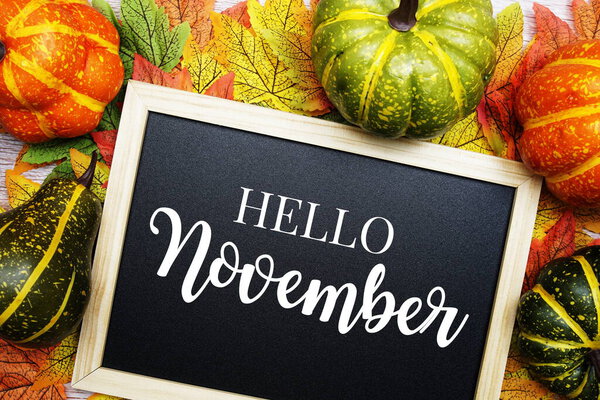 Hello November text on blackboard decorated with maple leaves on wooden background