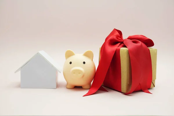 House model with piggy saving and gift box on pink background
