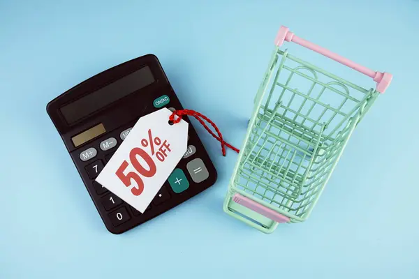 Top view of Sale 50% text on tag sale with calculator and shopping trolly cart flat lay on blue background