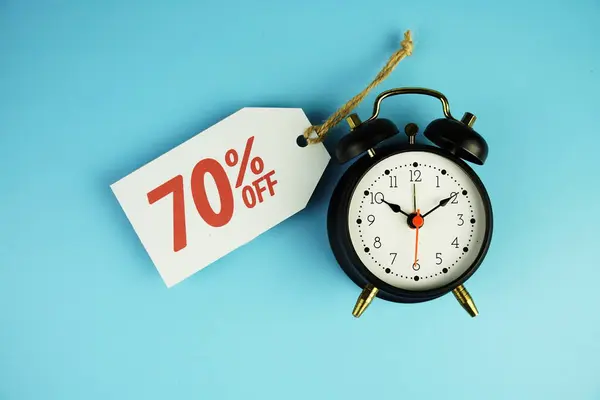 Top view of Sale 70% text on tag sale with black alarm clock flat lay on blue background