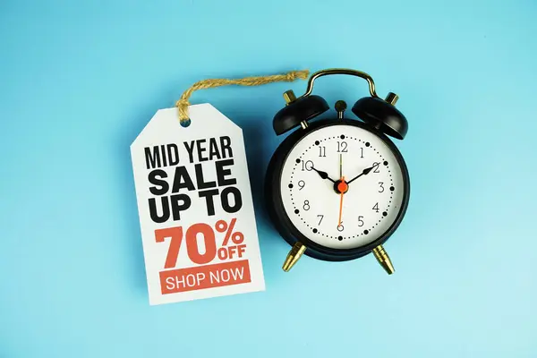 Top view of Mid year Sale 70% text on tag sale with black alarm clock flat lay on blue background