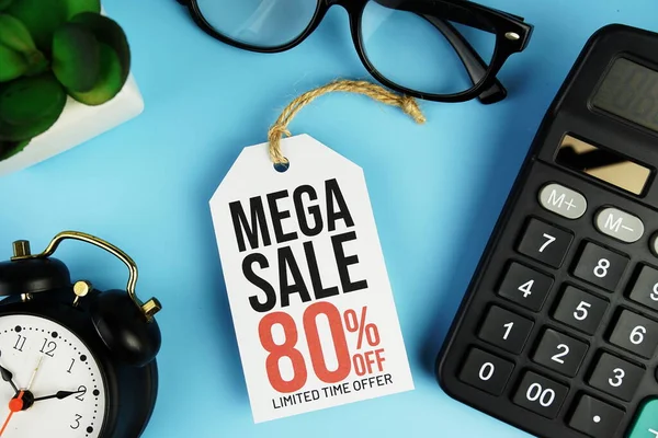 Top view of Mega Sale 80% text on tag sale with calculator and black alarm clock flat lay on blue background