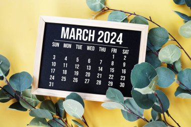 Sarı zemin üzerinde yeşil yaprak süslemesi bulunan 2024 Mart takvimi
