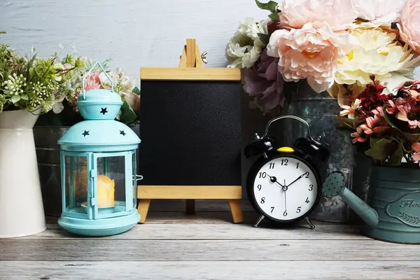 Mavi fener, çalar saat ve çiçek desenli ahşap arka planda Easel modeli.