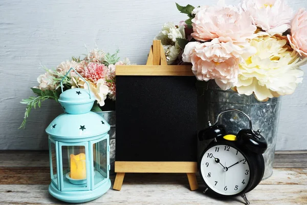 Mavi fener, çalar saat ve çiçek desenli ahşap arka planda Easel modeli.