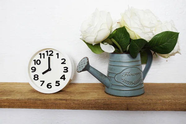 Ev dekorasyonu aksesuarları beyaz çalar saat ve tahta raflarda metal vazodaki çiçek ve beyaz beton duvar