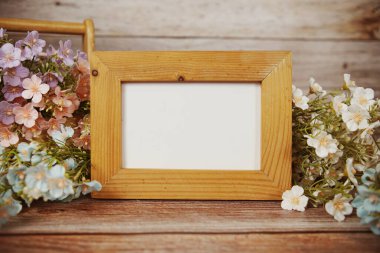 Boş fotoğraf çerçevesi ahşap arka planda çiçek buketi süslemesiyle maket yap