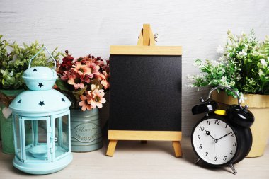 Mavi fener, çalar saat ve çiçek desenli ahşap arka planda Easel modeli.