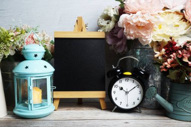 Mavi fener, çalar saat ve çiçek desenli ahşap arka planda Easel modeli.
