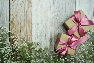 Pembe kurdeleli hediye kutuları ve tahta arka planda çiçek süslemeleri.