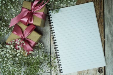 Not defteri ve hediye kutusunda pembe kurdele ve ahşap arka planda çiçek süslemesi.