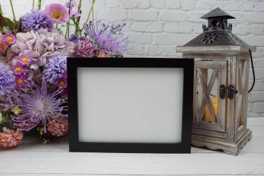 Boş fotoğraf çerçevesi çiçek buketi ve ahşap arka planda ev dekorasyonları ile modellenir.