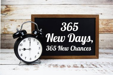 365 Yeni Gün 'den ilham verici bir alıntı. Tahtaya yeni şans metni yazılmış. Ahşap zemin üzerinde çalar saat var.