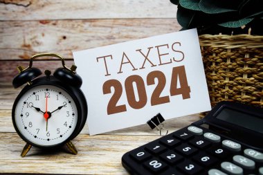 Ahşap zemin üzerinde alarm saati ve hesap makinesi olan 2024 vergisi metni