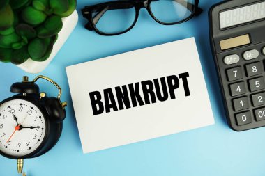 Alarm saati ve mavi arkaplanda hesap makinesi görünümlü kağıt kart üzerindeki iflas metni