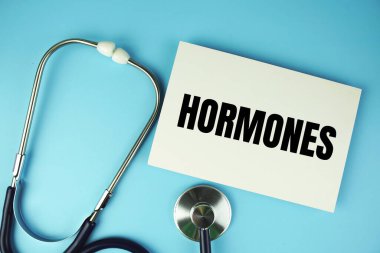 Mavi arkaplanda steteskop üst görünümü olan kağıt kart üzerindeki hormonlar metni