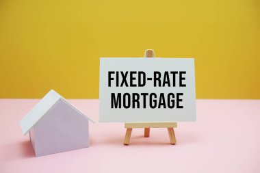 Sarı ve pembe arkaplan üzerine sehpa ve ev modeli içeren sabit faizli ipotek metni, Finansal ve Emlak kavramı
