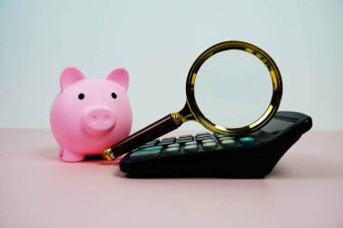 Magnifying glass on Calculator with piggy saving on pink background, Business and saving concept clipart