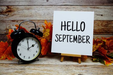 Merhaba Eylül metni, alarm saati ve ahşap arka planda akçaağaç yaprağı süslemesi.