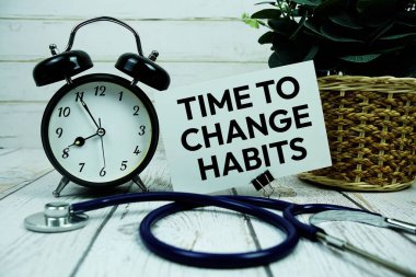 Time to Change Habits text on paper card with alarm clock and stethoscope on wooden background clipart