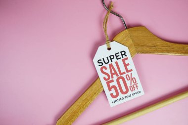 % 50 indirimli fiyat etiketi, ahşap elbise askısı pembe arka planda üst görünüm.