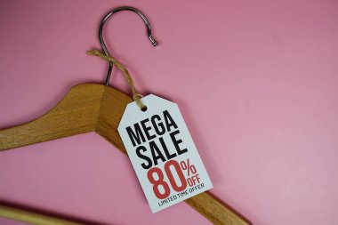 Fiyat etiketinde% 80 indirim, ahşap elbise askısı, pembe arka planda üst görünüm.