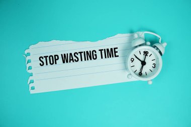 Stop Wasting Time quotes text on paper torn with alarm clock top view on blue background clipart