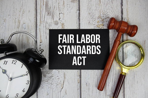 Fair Labor Standards Act text on paper card with alarm clock and wooden judge gavel top view on wooden background