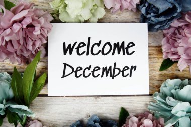 Ahşap arkaplanda çiçek çerçeveli kağıt kart üzerindeki Aralık ayına hoş geldiniz metni