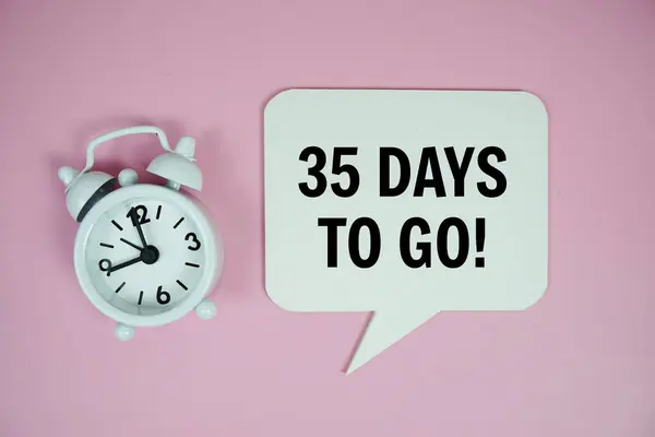 Stock image 35 Days to go text on speech bluble with alarm clock top view on pink background