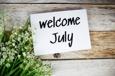 Tahta arka planda çiçek çerçeveli kağıt kart üzerindeki Temmuz ayına hoş geldiniz metni