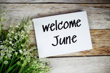 Kağıt kart üzerinde, çiçek çerçeveli, tahta arka planda Haziran ayına hoş geldiniz metni