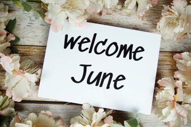 Kağıt kart üzerinde, çiçek çerçeveli, tahta arka planda Haziran ayına hoş geldiniz metni