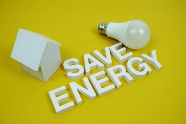 Ev modeli ve sarı zemin üzerindeki LED ampulleri, tasarruf ve çevre dostu kavramı içeren Enerji alfabesi harflerini kaydet
