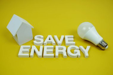 Ev modeli ve sarı zemin üzerindeki LED ampulleri, tasarruf ve çevre dostu kavramı içeren Enerji alfabesi harflerini kaydet