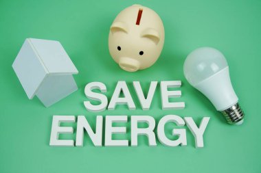 Ev modeli, domuz kumbarası ve yeşil arka planda LED ampulleri, Tasarruf ve Çevre dostu kavram içeren Enerji alfabesi harflerini kaydet