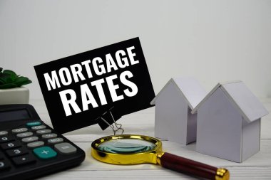 Ev modeli, hesap makinesi ve ahşap zemin üzerindeki büyüteçle İpotek Oranı metin iletisi