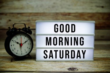 Günaydın cumartesi, LED ışık kutusu ve ahşap arka planda çalar saat.