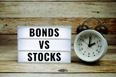 Tahta arka planda alarm saati, İş ve Para kavramının olduğu LED ışık kutusu üzerindeki tahvillere karşı senetler