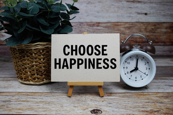 Choose Happiness text on paper card with alarm clock on wooden background