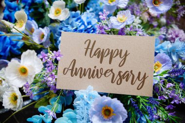 Mutlu yıldönümü metinleri kağıdın üzerine yazılır ve tahta arka planda çiçekler süslenir.